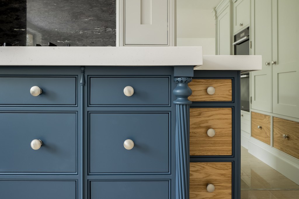 Close-up of a blue kitchen island with a turned corner post, white knobs and wooden drawers alongside
