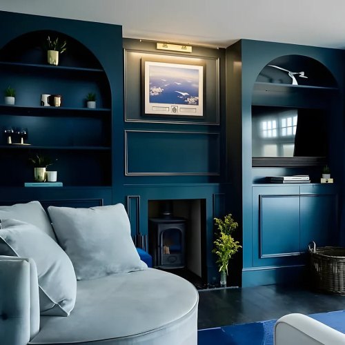 Dark teal living room with arched alcove shelving on each side of a fireplace and a TV in one alcove