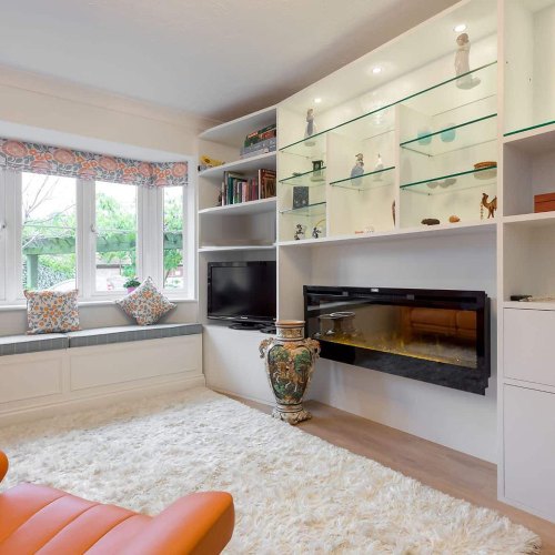 White built-in living room unit with glass display shelves and an inset fire beside a bay window