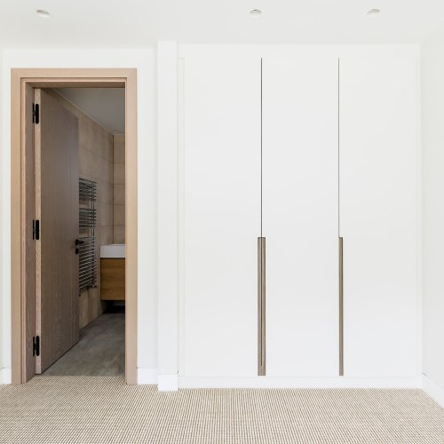 White floor-to-ceiling wardrobes with long bar handles beside an en-suite doorway
