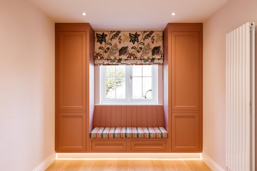Window seat with a striped cushion between two tall terracotta-coloured cupboards